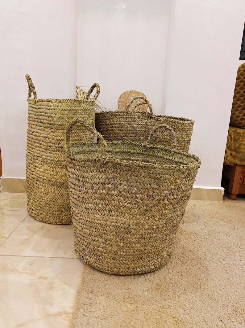 May include: Four woven seagrass baskets of varying sizes, with two of the baskets having handles. The baskets are sitting on a light brown rug.