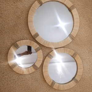 May include: Three round mirrors with natural woven frames, the largest mirror is in the center and the two smaller mirrors are on either side.