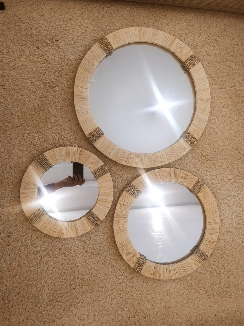 May include: Three round mirrors with natural woven frames, the largest mirror is in the center and the two smaller mirrors are on either side.