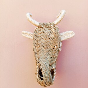 May include: A woven straw bull head wall hanging with white rope accents. The bull head is brown and has a hole in the center.