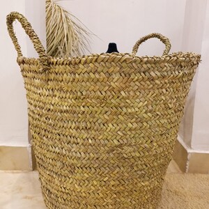 May include: A large, natural woven basket with two handles. The basket is made of a light brown, natural material and has a woven pattern.
