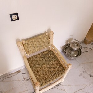 Pode incluir: Uma cadeira de palha tecida com uma estrutura de madeira. A cadeira est&aacute; sentada em um piso de ladrilhos brancos.