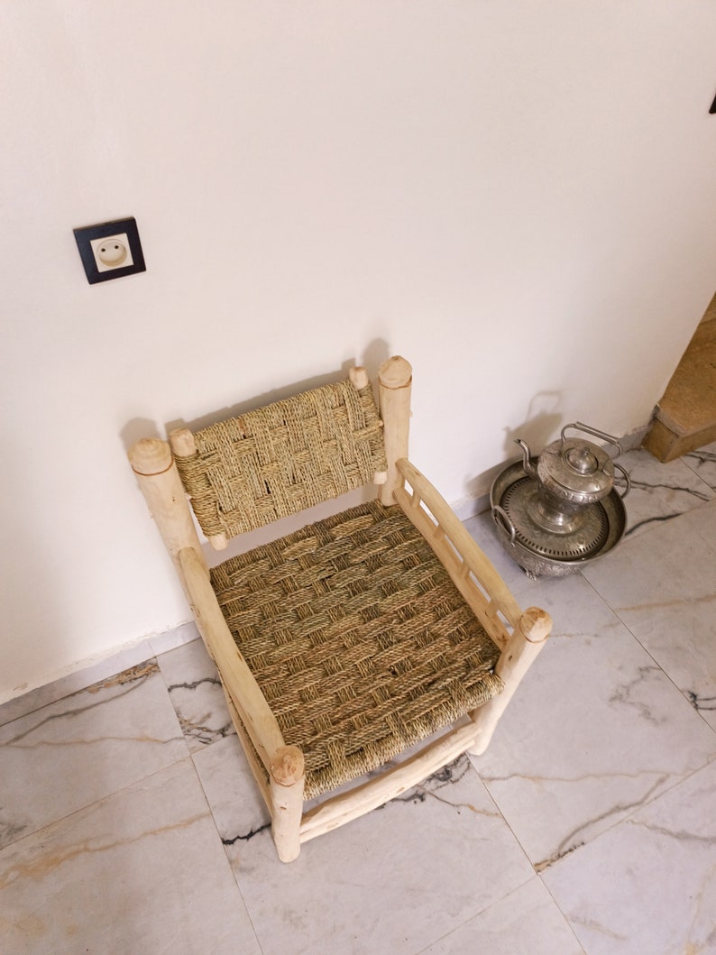 Pode incluir: Uma cadeira de palha tecida com uma estrutura de madeira. A cadeira est&aacute; sentada em um piso de ladrilhos brancos.