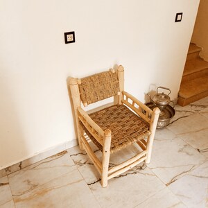 Pode incluir: Uma cadeira de madeira com assento e encosto de palha tran&ccedil;ada. A cadeira &eacute; de cor castanho claro e tem um design simples. A cadeira est&aacute; sentada num ch&atilde;o de ladrilhos brancos.