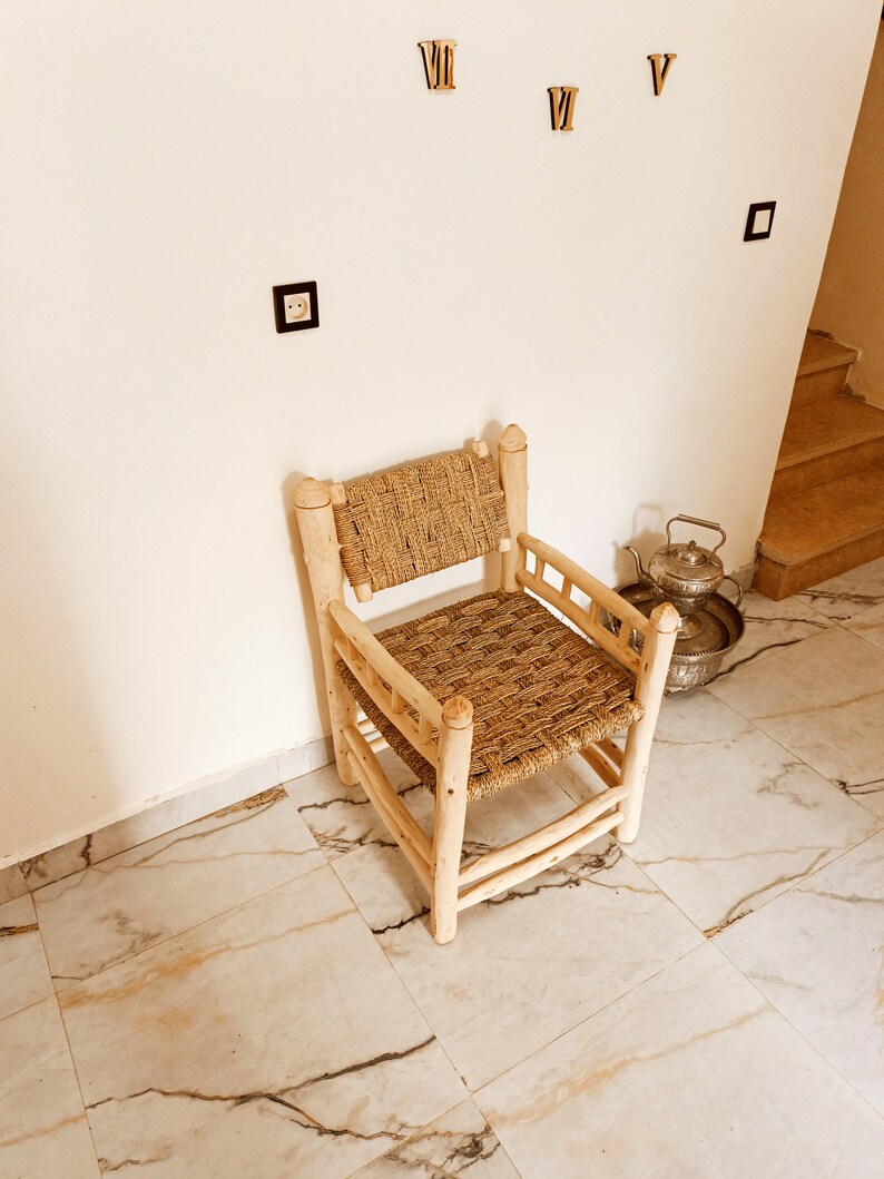 Pode incluir: Uma cadeira de madeira com assento e encosto de palha tran&ccedil;ada. A cadeira &eacute; de cor castanho claro e tem um design simples. A cadeira est&aacute; sentada num ch&atilde;o de ladrilhos brancos.
