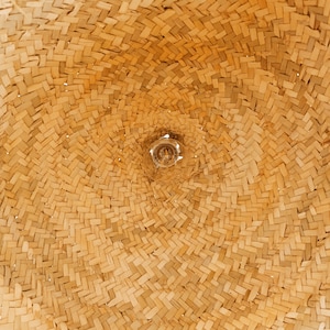 May include: Close-up of a woven straw lampshade with a light bulb visible in the center.