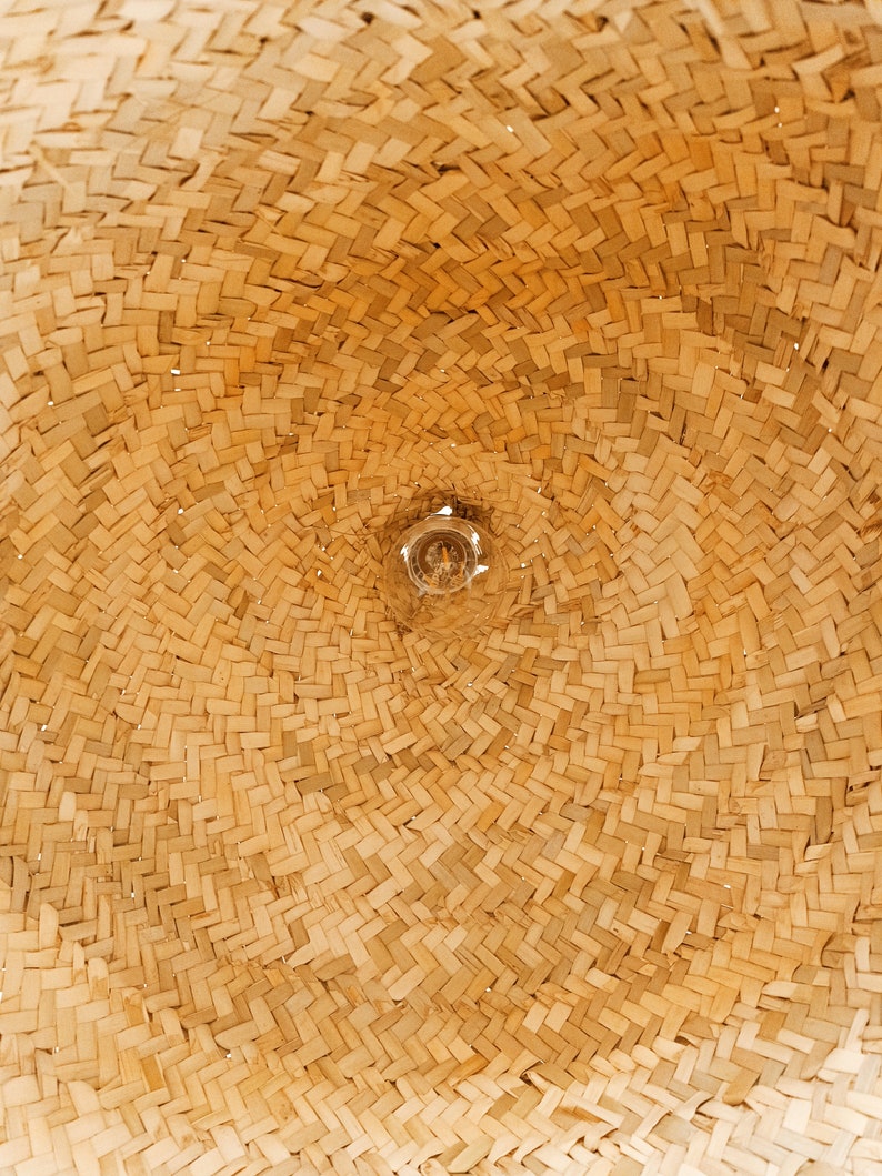 May include: Close-up of a woven straw lampshade with a light bulb visible in the center.