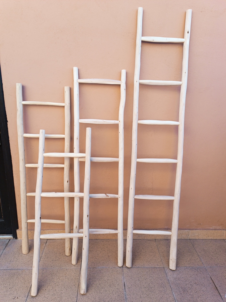 Puede incluir: Cuatro escaleras de madera blanca de diferentes alturas apoyadas en una pared de color melocot&oacute;n. Las escaleras tienen un aspecto r&uacute;stico y natural, perfectas para a&ntilde;adir un toque de estilo farmhouse a cualquier habitaci&oacute;n.