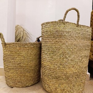 May include: Two woven seagrass baskets with handles. The larger basket is taller and has a wider opening than the smaller basket.