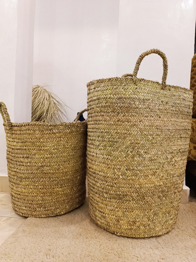 May include: Two woven seagrass baskets with handles. The larger basket is taller and has a wider opening than the smaller basket.