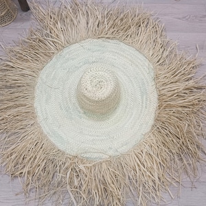 May include: A large, round straw hat with a wide brim and a fringe trim. The hat is made of natural straw and has a light brown color.