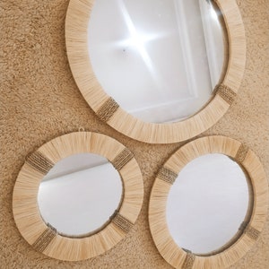 May include: Three round mirrors with natural woven frames. The mirrors are different sizes and are hanging on a beige wall.