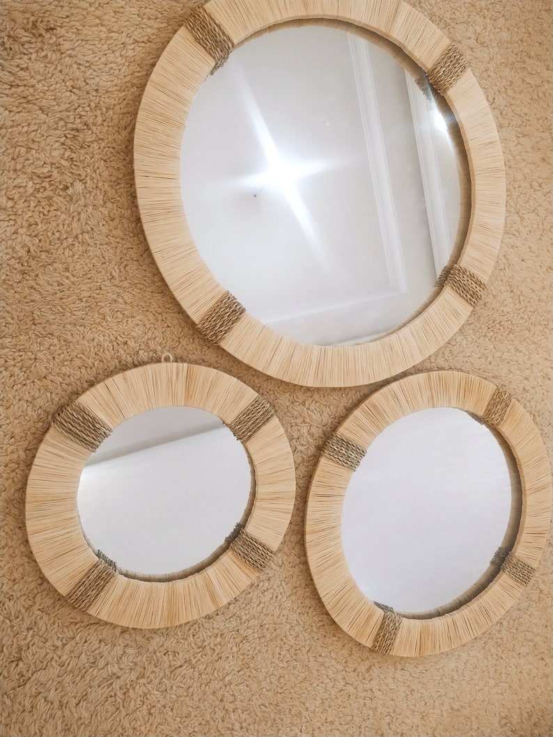 May include: Three round mirrors with natural woven frames. The mirrors are different sizes and are hanging on a beige wall.