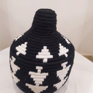 K&ouml;nnte beinhalten: Schwarze und wei&szlig;e gewebte Vase mit geometrischem Muster. Die Vase ist aus einem dicken, strukturierten Material gefertigt und hat eine runde Form.