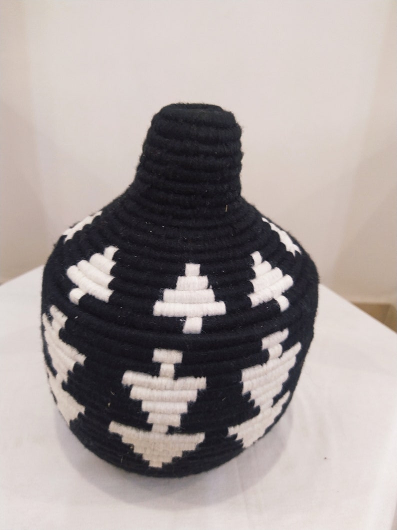 K&ouml;nnte beinhalten: Schwarze und wei&szlig;e gewebte Vase mit geometrischem Muster. Die Vase ist aus einem dicken, strukturierten Material gefertigt und hat eine runde Form.