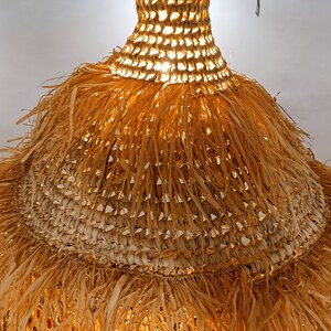 May include: A woven light fixture with a fringe made of natural fibers. The light fixture is round and has a light brown color.