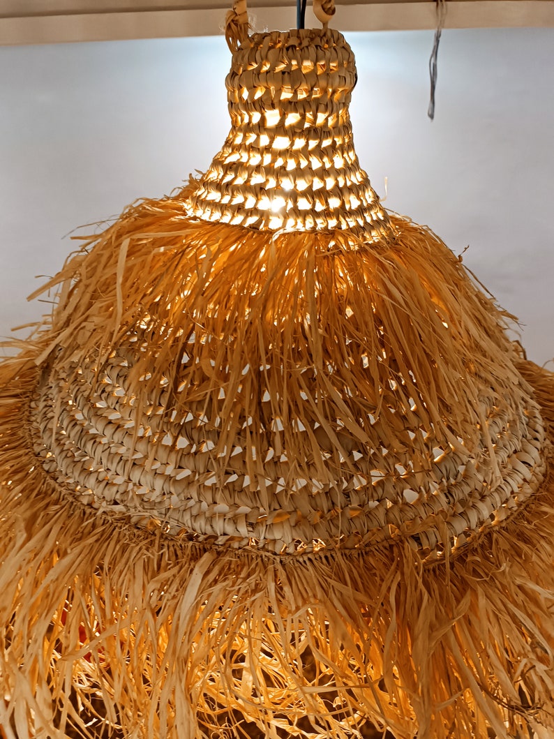 May include: A woven light fixture with a fringe made of natural fibers. The light fixture is round and has a light brown color.