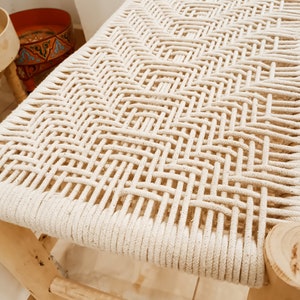 May include: A wooden stool with a woven white rope seat. The stool is made of natural wood and has a simple, rustic design.
