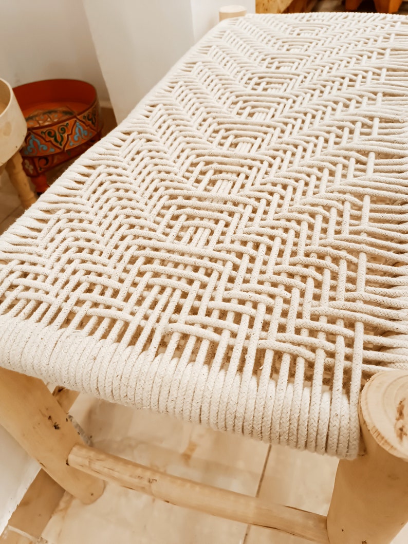 May include: A wooden stool with a woven white rope seat. The stool is made of natural wood and has a simple, rustic design.