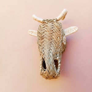 May include: A woven straw cow head wall hanging with white rope horns. The cow head is a light brown color and has a hole in the center of the face.