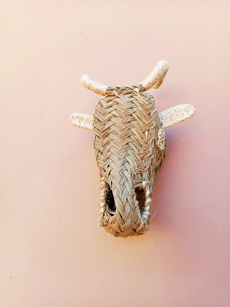 May include: A woven straw cow head wall hanging with white rope horns. The cow head is a light brown color and has a hole in the center of the face.