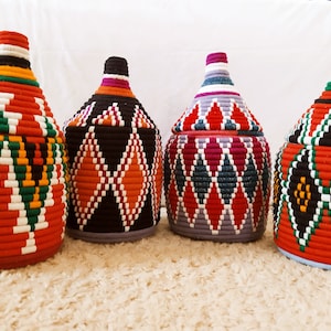 Peut inclure: Quatre paniers de rangement tissés avec des motifs géométriques colorés. Les paniers sont faits de fil rouge, blanc, vert, bleu, noir et orange.