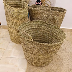May include: Three woven baskets made of natural materials. The baskets are different sizes and shapes, with two round baskets and one tall, cylindrical basket.