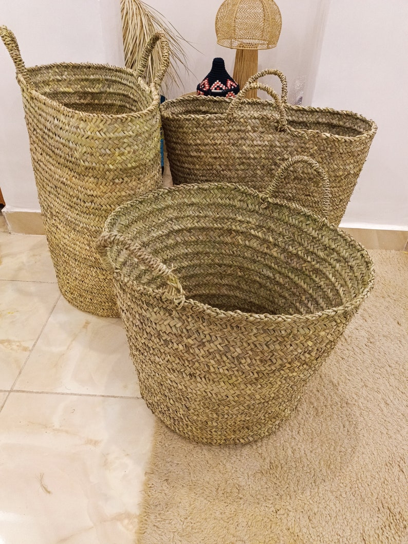 May include: Three woven baskets made of natural materials. The baskets are different sizes and shapes, with two round baskets and one tall, cylindrical basket.