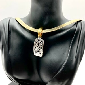 Op de afbeelding: Een gouden ketting met een zilveren hanger met een delicaat, ingewikkeld bloemmotief.