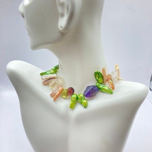 May include: A multi-coloured necklace featuring green, purple, brown and white stones. The necklace is crafted from a variety of materials, including pearls, shells and crystals.