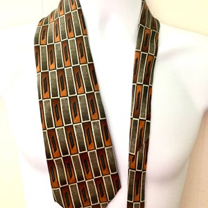 Op de afbeelding: Een stropdas met een patroon met een herhalend rechthoekig ontwerp in bruin-, grijs- en groentinten. De stropdas wordt getoond op een witte mannequin, die het geometrische patroon en kleurenpalet benadrukt. Een klassiek, veelzijdig accessoire.