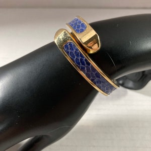 May include: A gold and blue snake-shaped bangle bracelet. The bracelet is made of metal and has a blue leather-like finish.
