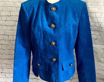 May include: A bright blue suede jacket with a round collar and four gold-coloured buttons. The jacket has two front pockets with matching gold buttons. The sleeves are long, and the jacket is displayed on a mannequin.