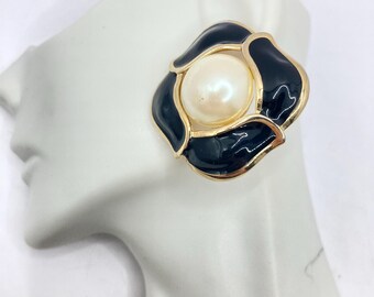 May include: Gold tone earrings with a black enamel flower design and a white pearl in the center.