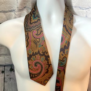 Peut inclure: Une cravate marron à motifs cachemire avec des accents dorés, roses et turquoise. La cravate est présentée sur un mannequin blanc. Le motif cachemire est complexe et détaillé, avec un design classique.