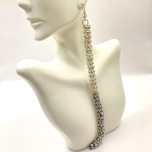 May include: Silver long dangle earrings with a beaded design. The beads are small and round, and they are arranged in a spiral pattern. The earrings are very long, and they would be a statement piece.