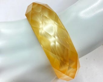May include: A yellow, faceted, plastic bangle bracelet. The bracelet is made of a translucent material with a shiny finish.