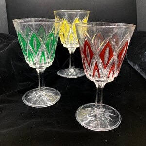 Puede incluir: Tres copas de vino transparentes con diseños en forma de diamante de colores. Una copa tiene detalles verdes, otra amarillos y la tercera rojos. Las copas tienen un tallo clásico y una base en forma de estrella, ideales para servir vino.