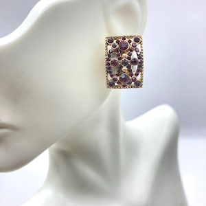 May include: Gold tone earrings with a rectangular design featuring a geometric pattern of red rhinestones.