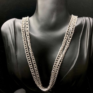 May include: Silver-toned chain necklace with a curb link design. The necklace is displayed on a black mannequin, showcasing the multiple strands and the intricate details of the chain. The jewelry is a classic accessory.