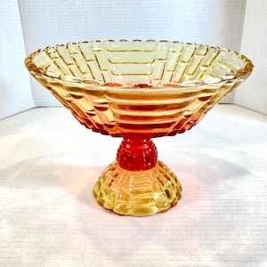 May include: A vintage glass bowl with a pedestal base. The bowl is yellow and orange with a red base. The bowl has a textured design.