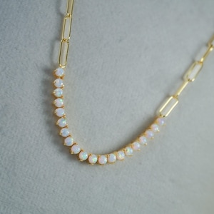 May include: A gold-toned necklace featuring a chain with elongated rectangular links on the upper sections and a central curved segment composed of small, round, iridescent white opal-like stones set in individual gold-toned metal prongs.