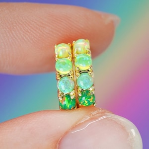 May include: A pair of gold hoop earrings featuring a vertical row of four round cabochon opals on each piece. The opals display a gradient of colors, transitioning from pale yellow and light green at the top to deep emerald green at the bottom.