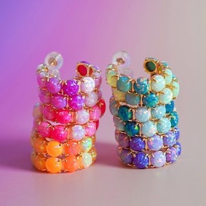 May include: Two hoop earrings featuring rows of round, prong-set cabochon stones. The left earring displays a gradient of warm colors including orange, pink, and magenta. The right earring features a gradient of cool colors including blue, teal, and purple.