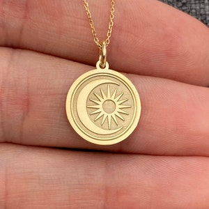 Może przedstawiać: Złoty naszyjnik z okrągłym wisiorem przedstawiającym półksiężyc i słońce.
