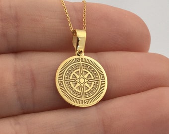 May include: A gold-colored pendant necklace featuring a circular compass design. The pendant is round with an engraved compass rose pattern and hangs from a delicate gold chain. The necklace is displayed against a neutral background.