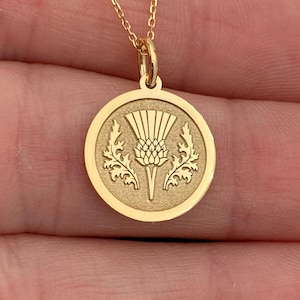 May include: A gold chain necklace with a round pendant featuring a detailed engraving of a thistle flower.