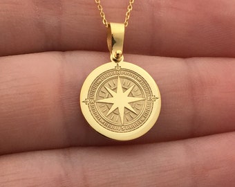 May include: A gold pendant necklace with a compass design. The round pendant has an engraved compass rose and hangs from a fine chain. The necklace is shown against a plain background.