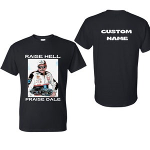Op de afbeelding: Zwart T-shirt met een witte afbeelding van Dale Earnhardt Jr. en zijn raceauto. De tekst "Raise Hell Praise Dale" is op het shirt gedrukt. De achterkant van het shirt heeft de tekst "Custom Name" in wit gedrukt.