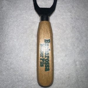 May include: A wooden bottle opener with a silver top. The handle is engraved with the text "Barossa Beer Pils".